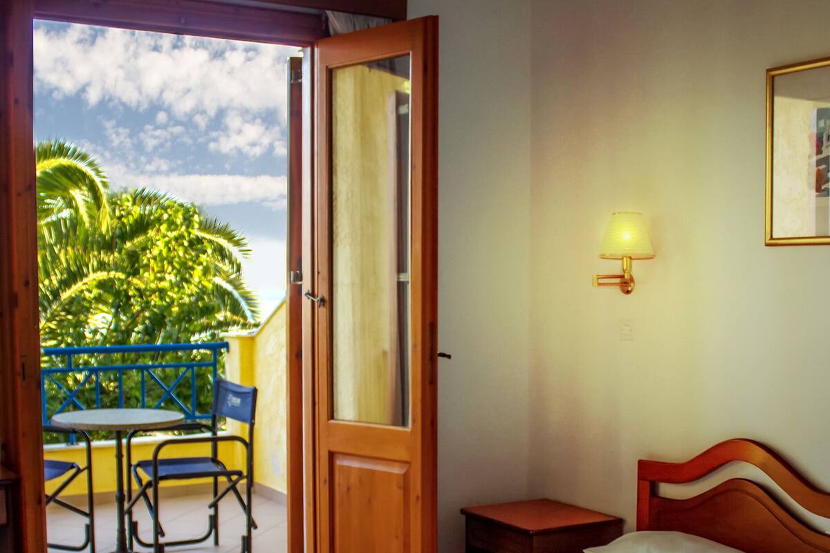 A hotel room with two beds, a balcony with a table and chairs, and a ceiling fan.