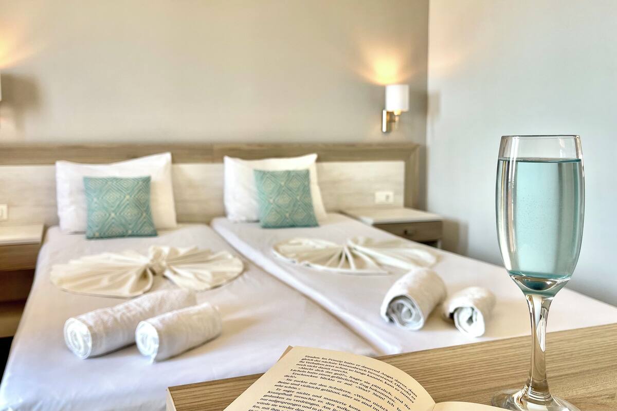 A neatly made bed with towels, a glass of water, and a book on a bedside table in a hotel room.