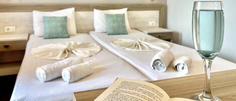 A neatly made bed with towels, a glass of water, and a book on a bedside table in a hotel room.