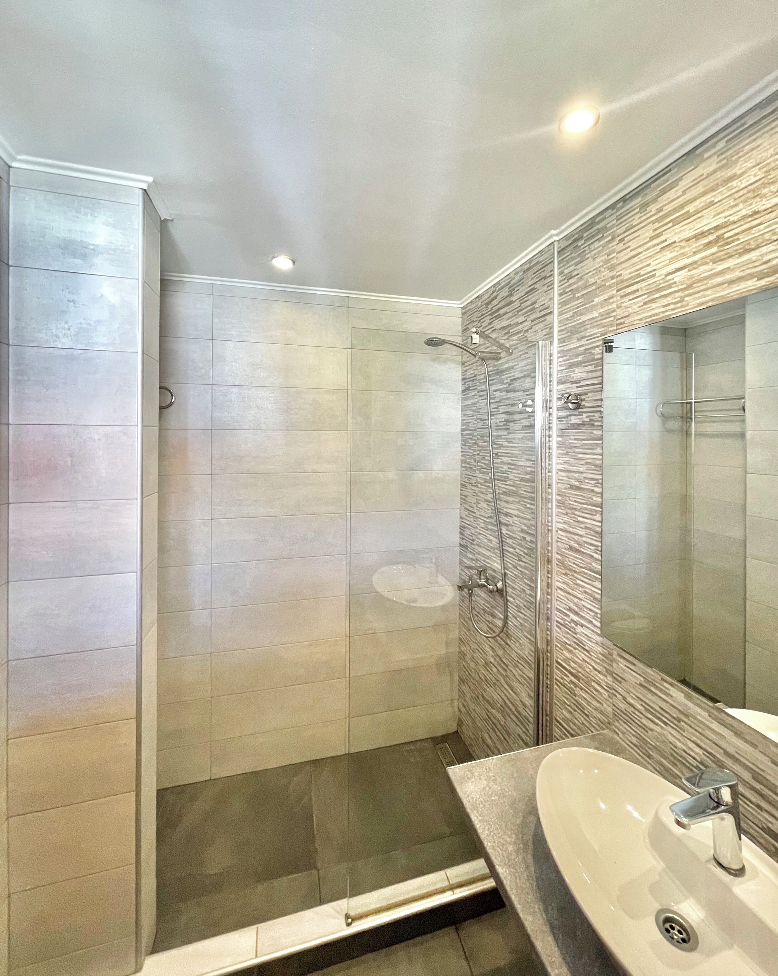 A modern bathroom with a walk-in shower, a vanity with a sink, and a large mirror.