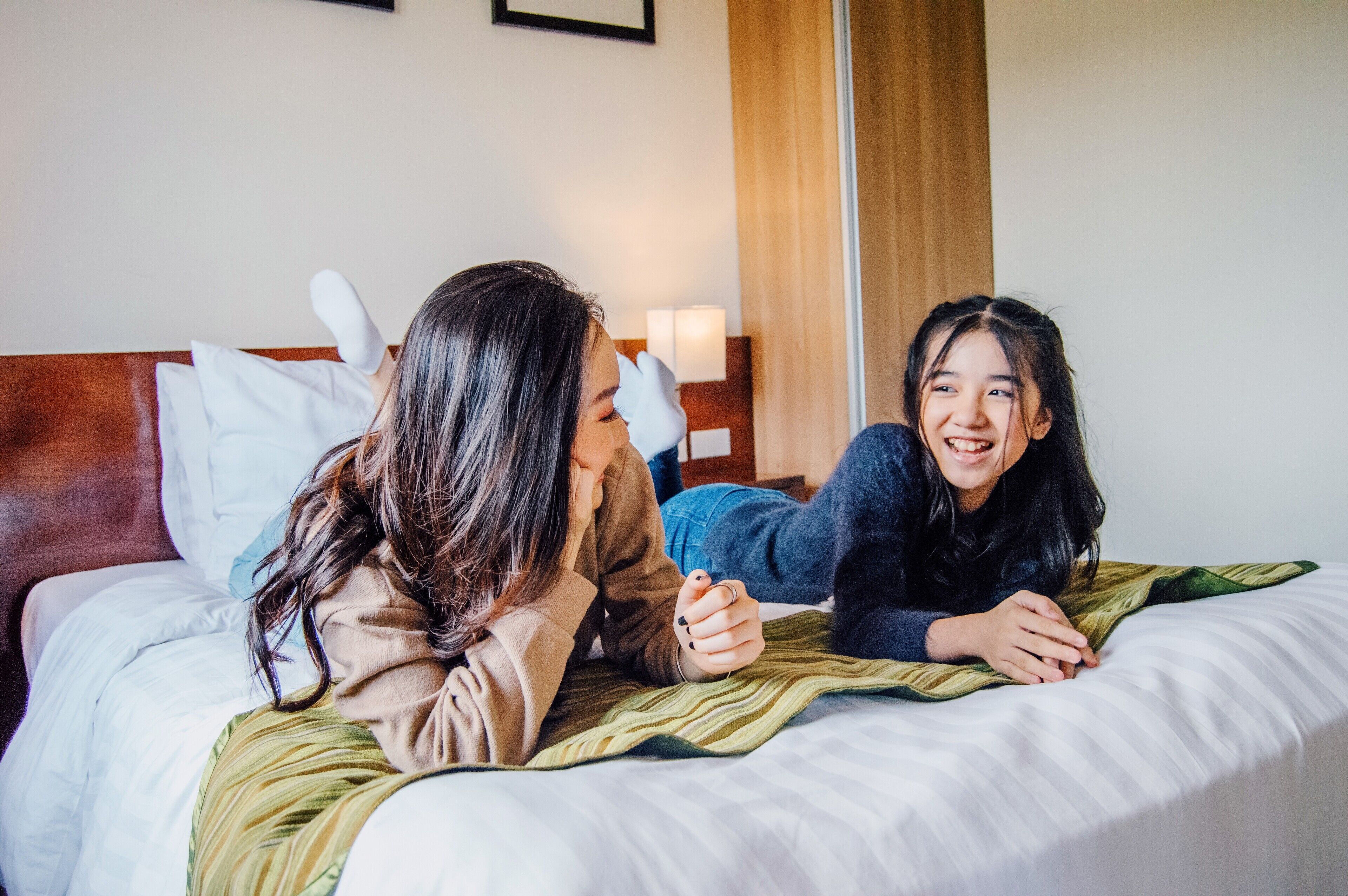 Two people lying on a bed with a wooden headboard, a green blanket, and a white pillow.