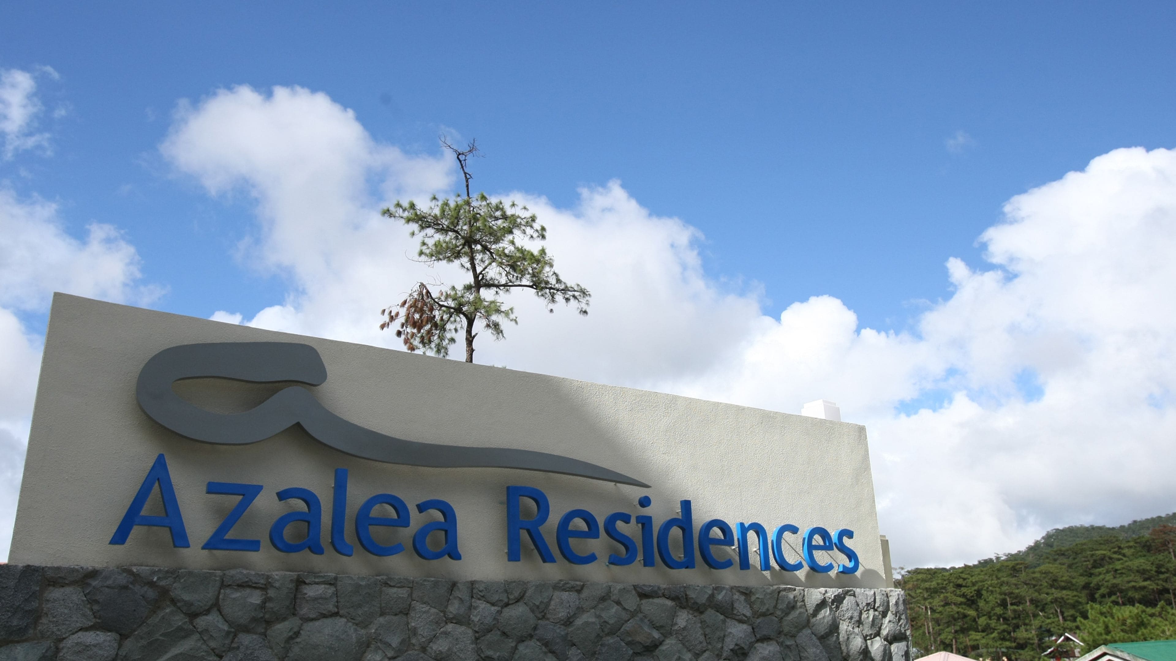 Bordje voor Azalea Residences, met een gestileerd golvend ontwerp en een boom op de achtergrond.