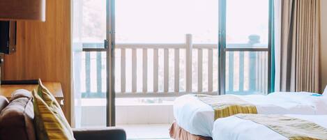 A hotel room with a bed, a sofa, a table, and a balcony with a railing.