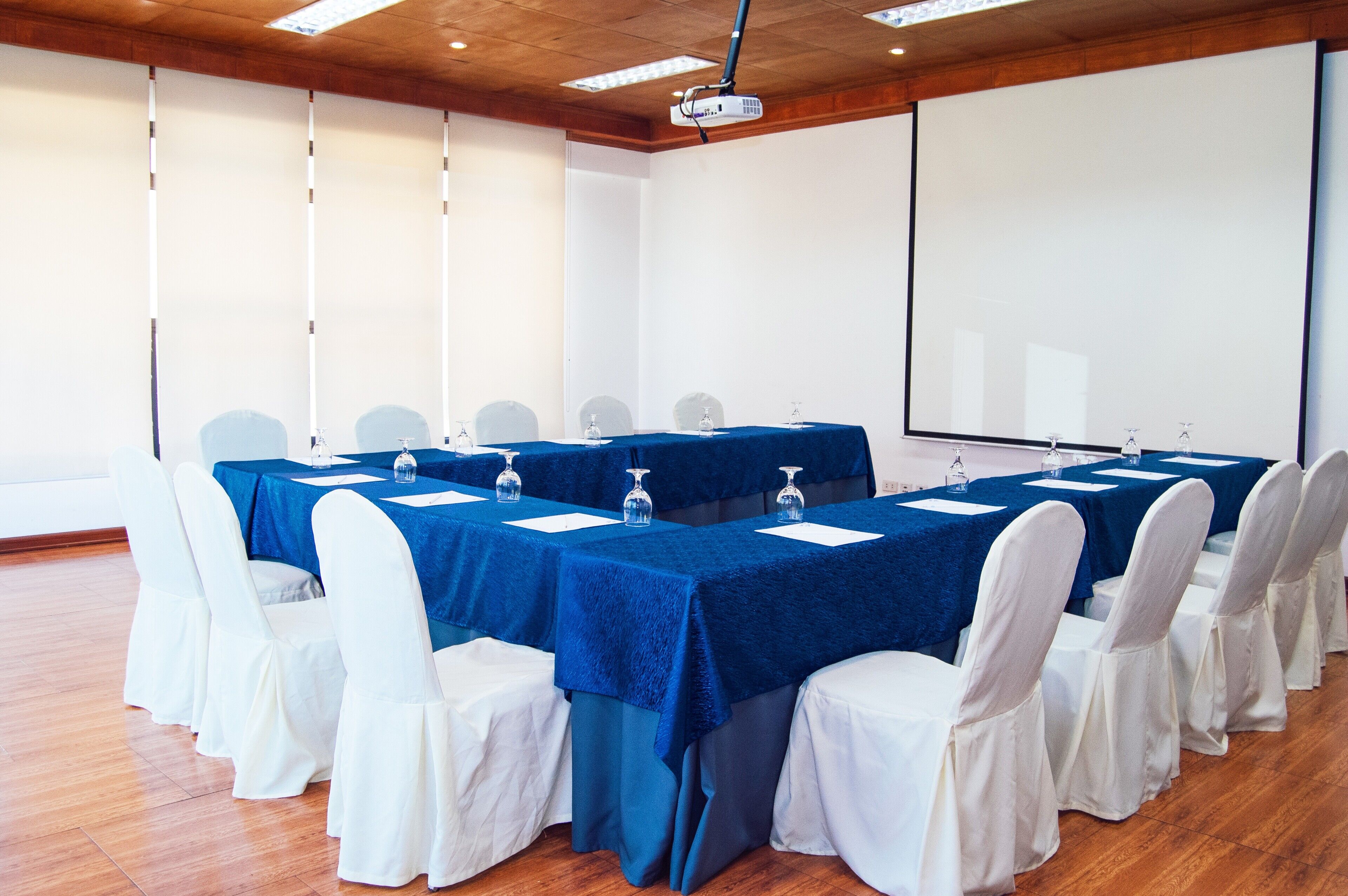A conference room with a long table, white chairs, and a projector screen.