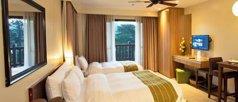 A hotel room with two beds, a desk, a chair, a television, and a balcony with a view of trees.
