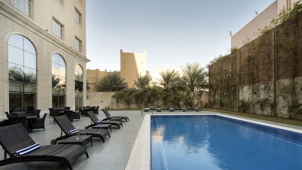 Zona de piscina con sillas de descanso y un edificio con grandes ventanales.