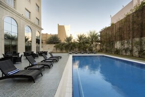 A swimming pool area with lounge chairs and a building with large windows.