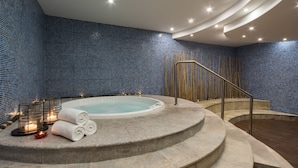 Un área de spa con un jacuzzi, escalones de piedra, velas y una pared de mosaico azul.