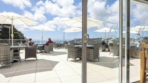 Un patio al aire libre con mobiliario de mimbre, sombrillas blancas y vistas al mar.