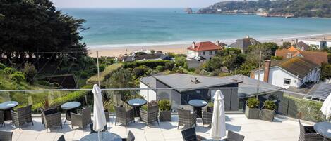 Una terraza con mobiliario de mimbre y sombrillas, con vistas a una playa y al océano.
