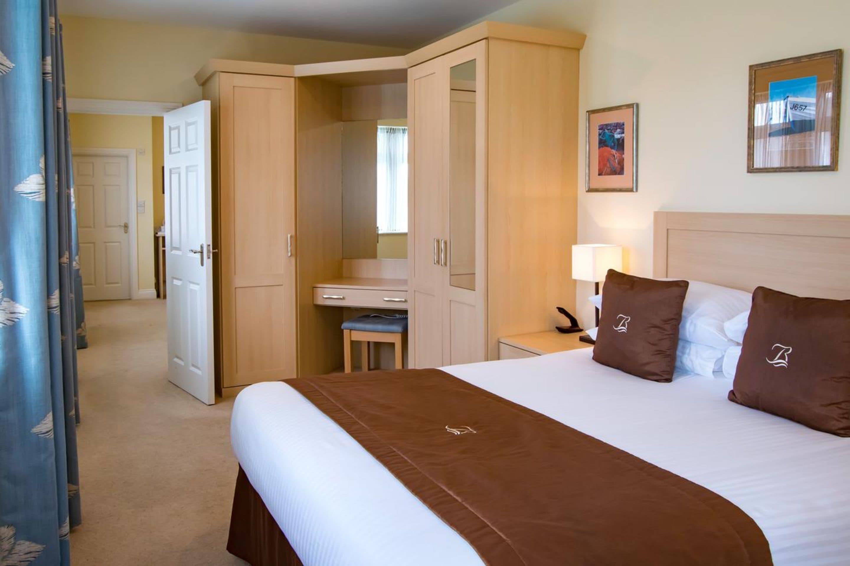 A hotel room with a large bed, a desk, and a wardrobe.