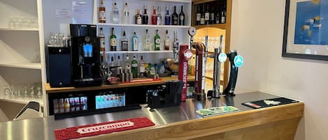 A bar area with a variety of liquor bottles, a coffee machine, and a digital screen displaying the menu.