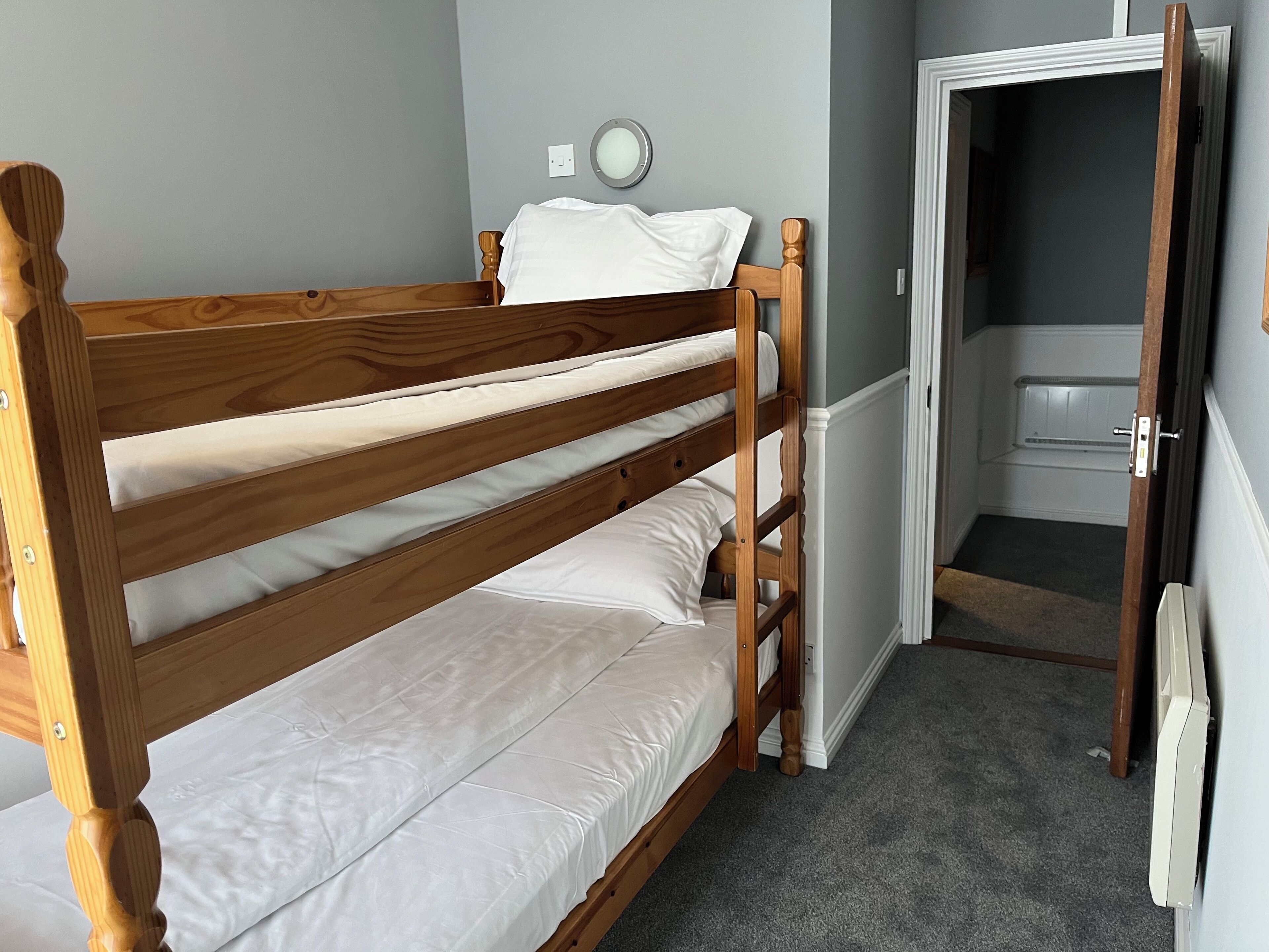 Una cama individual con ropa blanca en una habitación con paredes grises y suelo alfombrado.