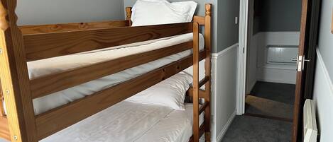 Una cama individual con ropa blanca en una habitación con paredes grises y suelo alfombrado.