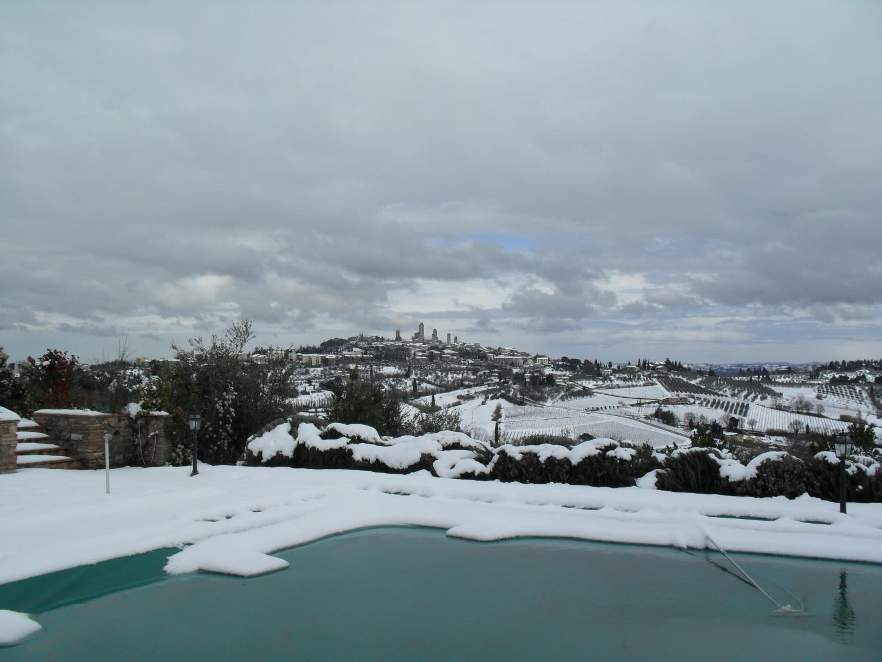 Paesaggio innevato con area piscina e edifici in lontananza.