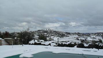 Paesaggio innevato con area piscina e edifici in lontananza.