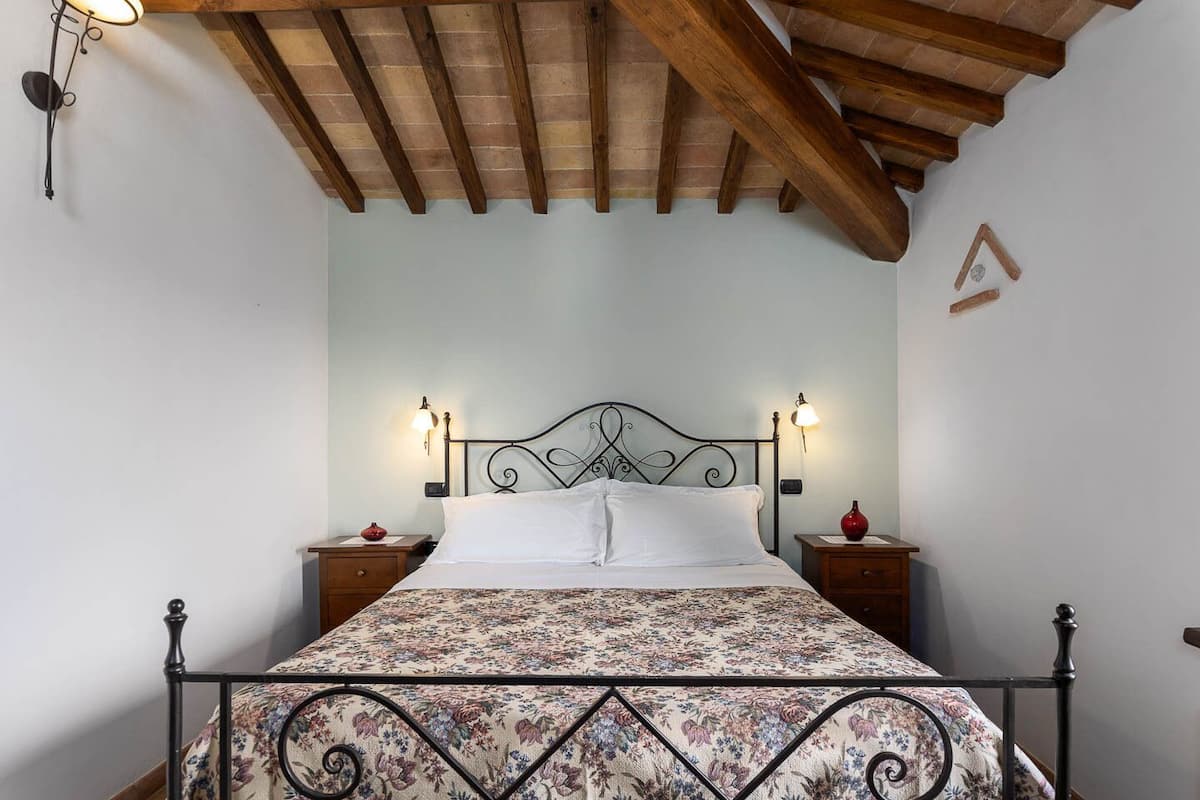Quarto com uma cama, duas mesas de cabeceira e teto de madeira.