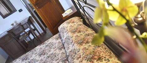 Una cama con ropa de cama floral, una mesita de noche de madera, un espejo y una puerta.