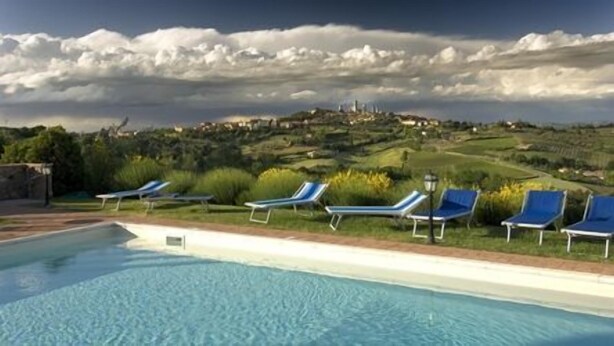 A swimming pool with lounge chairs and a view of a hill with buildings. - Agriturismo Il Casolare di Bucciano (San Gimignano)