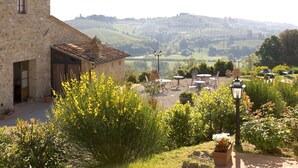 A stone building with a terrace, outdoor seating, and a view of rolling hills. - Agriturismo Il Casolare di Bucciano (San Gimignano)