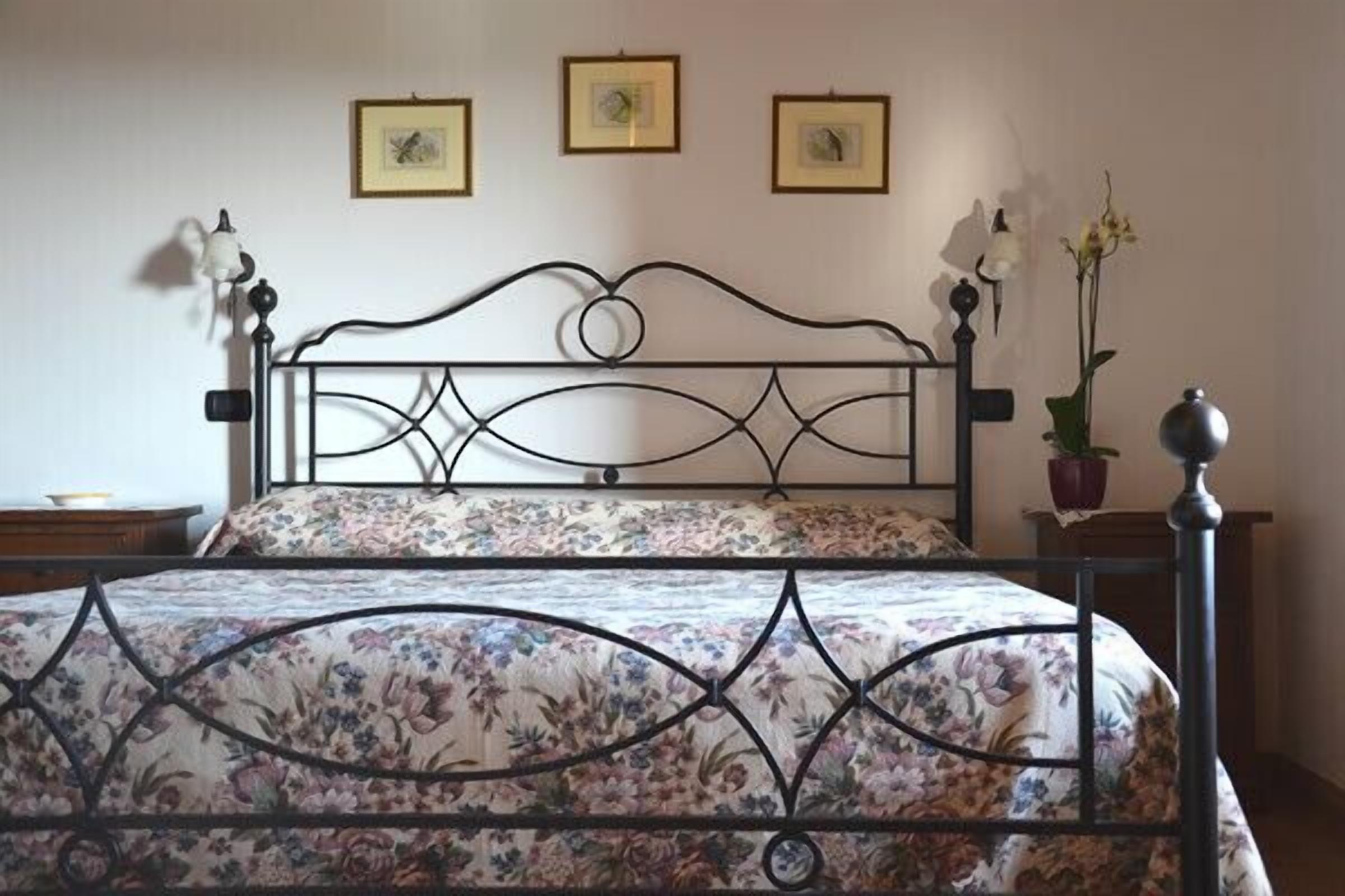 Una cama con colcha estampada de flores y cabecero de metal. Encima de la cama, en la pared, hay tres cuadros enmarcados.