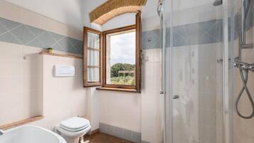 Une salle de bain avec une douche, des toilettes et une fenêtre dont le volet est ouvert.