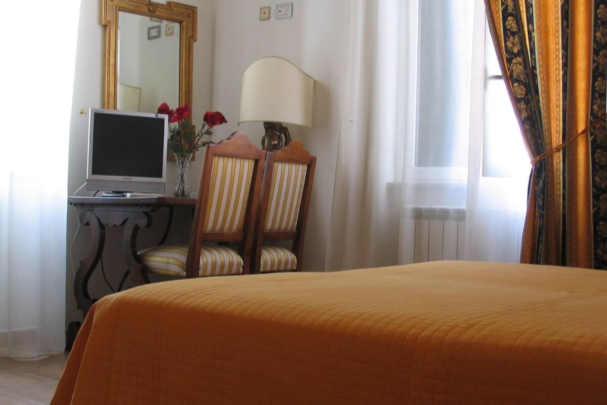 A hotel room with a bed, a desk with a laptop, a mirror, and a lamp.