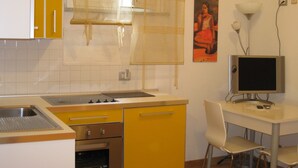 A compact kitchen with yellow cabinets, a white countertop, a sink, a stove, and a small dining area with a chair and a table. - La Rotella nel Sacco (Rome)