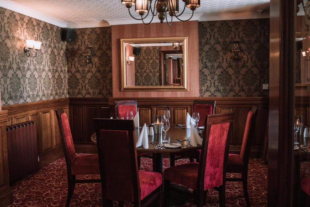 Une salle à manger élégante avec un mur lambrissé en bois, un grand miroir et des chaises recouvertes d’un tissu rouge.