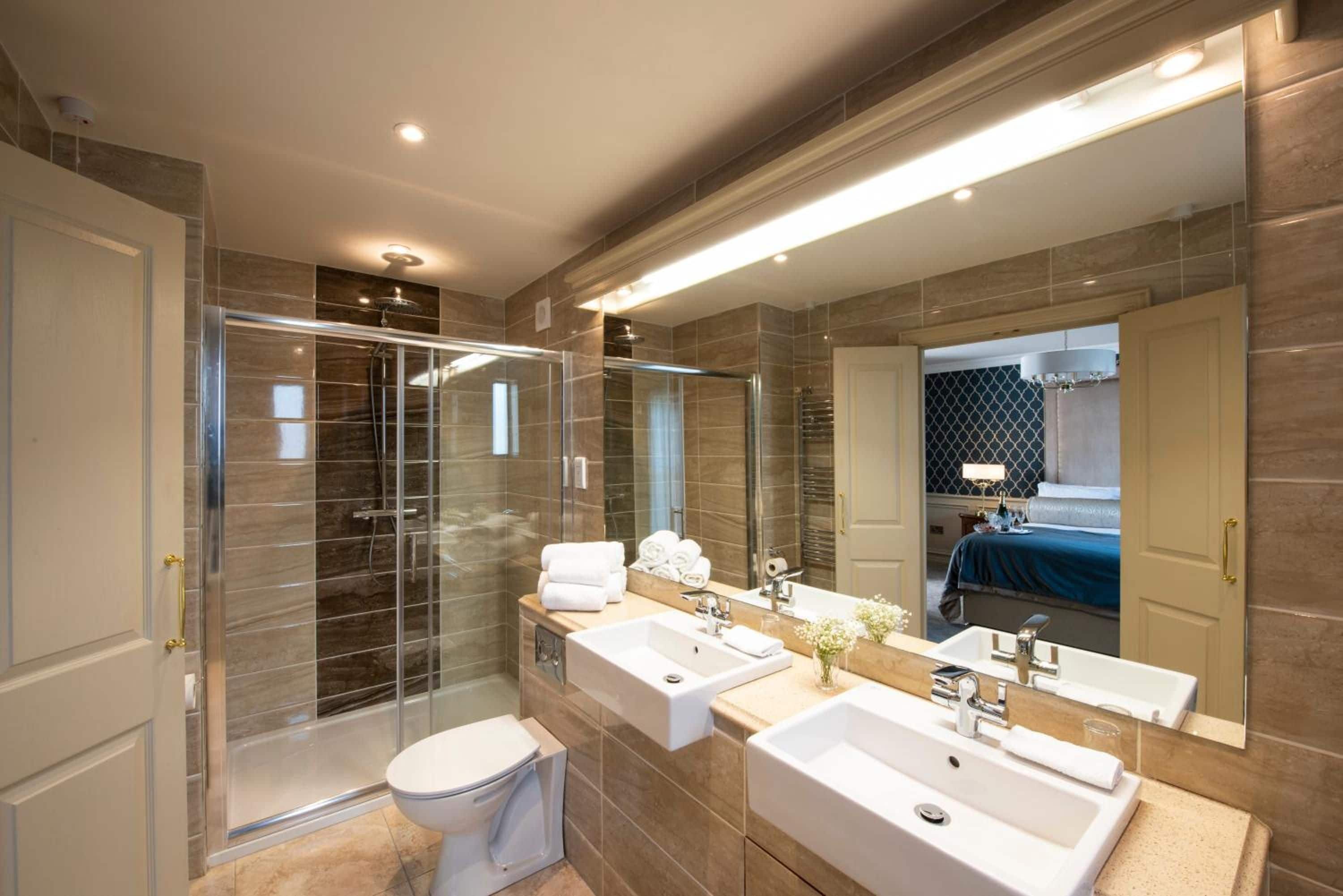 Un baño moderno con cabina de ducha de vidrio, dos lavamanos y un espejo grande.