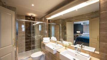 Un baño moderno con cabina de ducha de vidrio, dos lavamanos y un espejo grande.