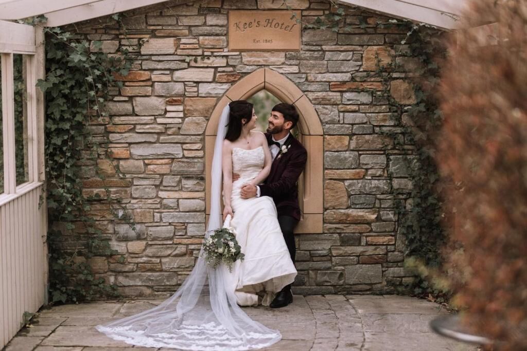 A stone wall with a sign that reads 'Kee's Hotel' and a couple embracing.