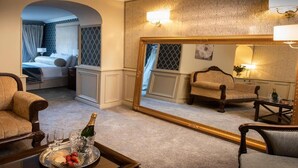 Habitación de hotel con sofá, sillón y una mesa de comedor con una botella de champán y fruta.