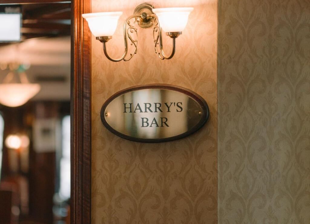 Un letrero en la pared con la inscripción 'HARRY'S BAR', flanqueado por dos apliques.