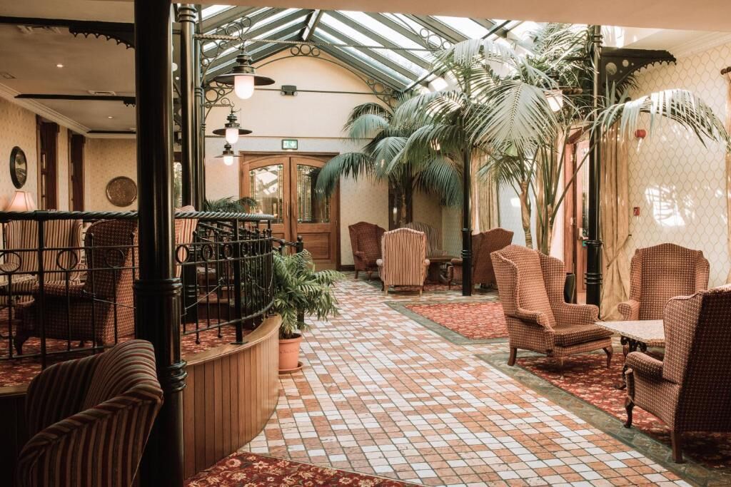 Um saguão de hotel com piso de azulejos, móveis de vime e teto de vidro.