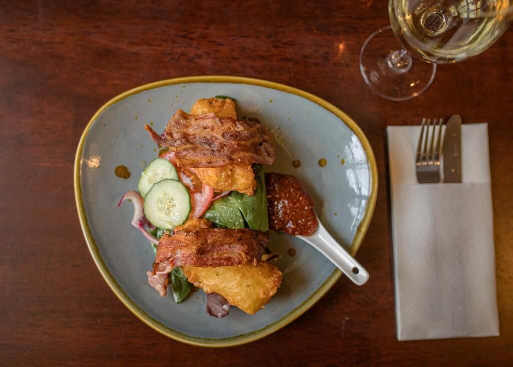 A plate of food with a fork and knife on a napkin, and a glass of white wine on the table.