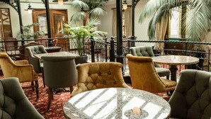 Un vestíbulo de hotel con mesas y sillas redondas, una alfombra roja y plantas grandes en macetas.