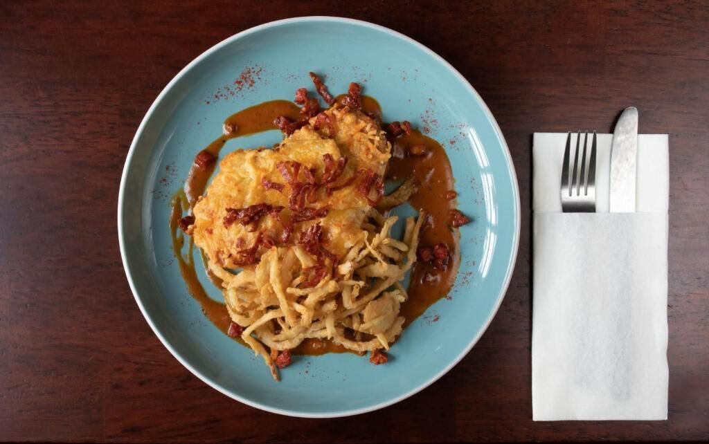 A plate of food with a blue rim, accompanied by a white napkin and cutlery on a wooden table.