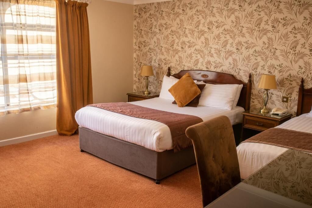 A hotel room with a large bed, two bedside tables, a chair, and a patterned wallpaper.