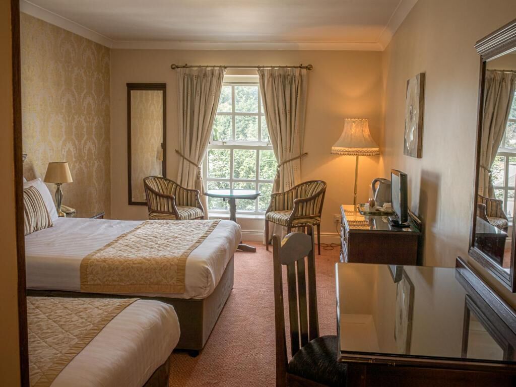 A hotel room with a bed, two chairs, a desk, a lamp, and a television.
