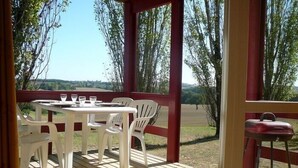 Un espace de restauration extérieur abrité, doté d’une terrasse en bois, de chaises en plastique blanches et d’une table dressée pour deux personnes.