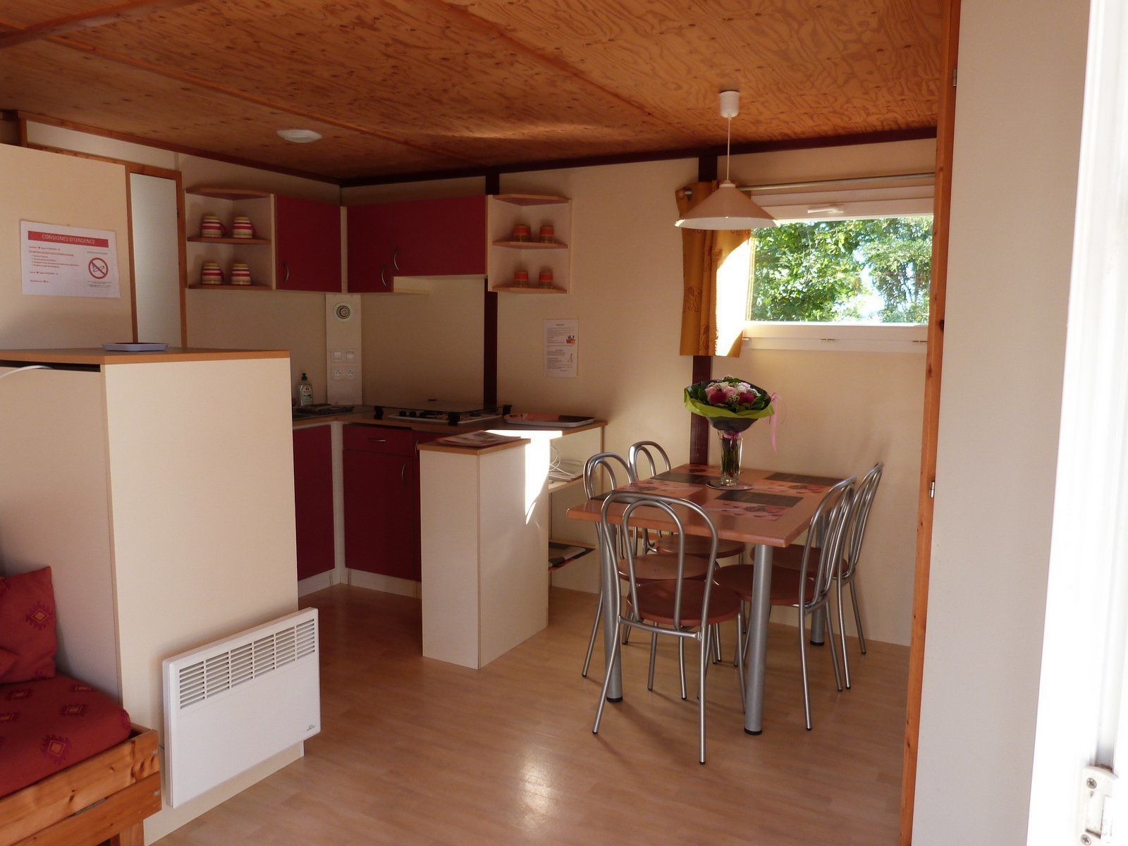 Cocina compacta con zona de comedor, techo de madera y ventana con vista a follaje.