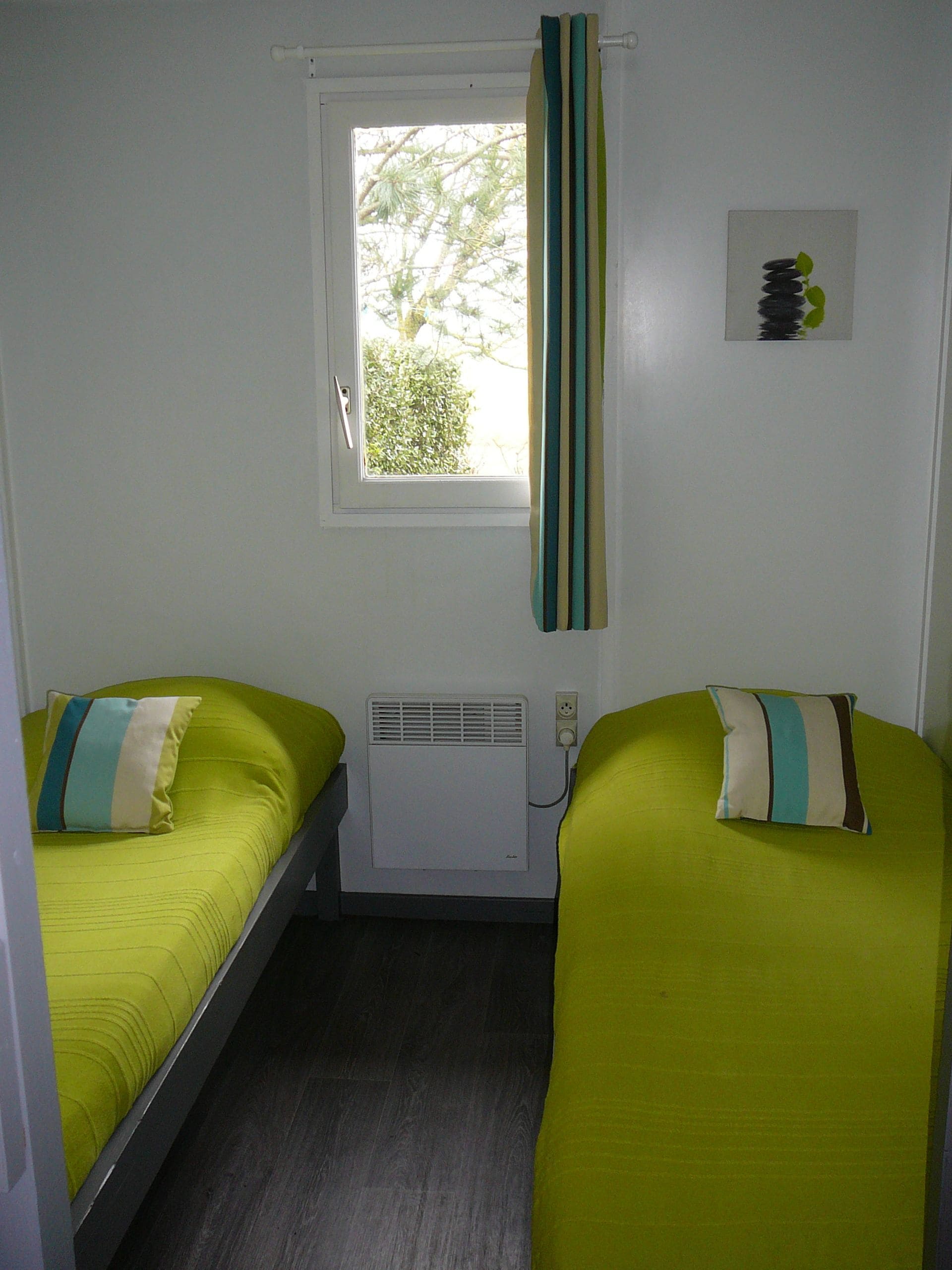 A small room with two single beds, a window with curtains, a wall-mounted air conditioner, and a power outlet.