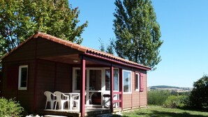 Une petite cabane en bois avec un porche, des chaises en plastique blanc et une vue sur le paysage environnant.