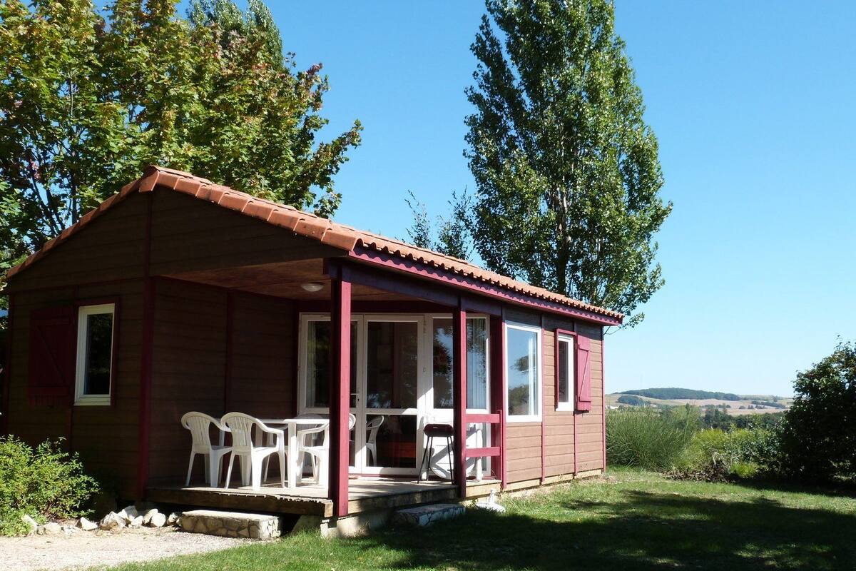 Een klein houten huisje met een veranda, witte plastic stoelen en uitzicht op het omliggende landschap.