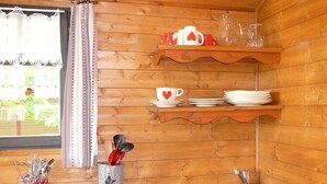 Une cuisine rustique aménagée dans une cabane en bois, avec une fenêtre, un évier, une cuisinière et des étagères remplies de tasses et d’assiettes.