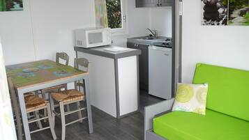 A compact kitchen with a microwave, sink, and small refrigerator. There is a dining table with chairs and a green sofa with a pillow.
