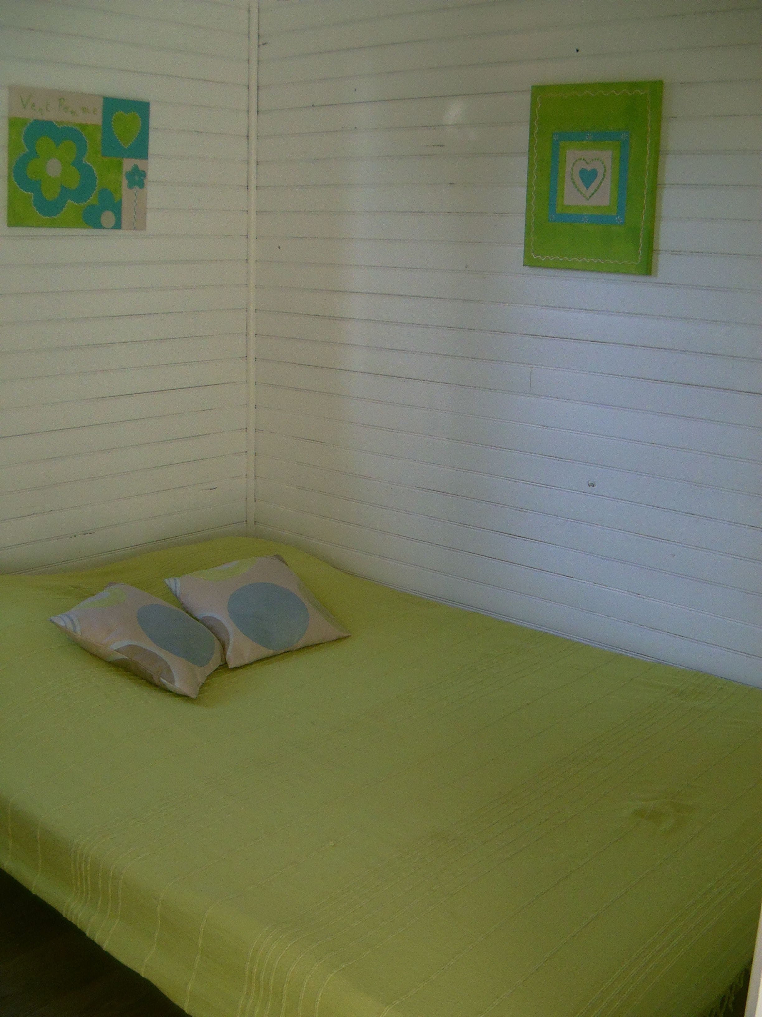 A small, single-bed room with a green bedspread, two pillows, and two wall decorations.