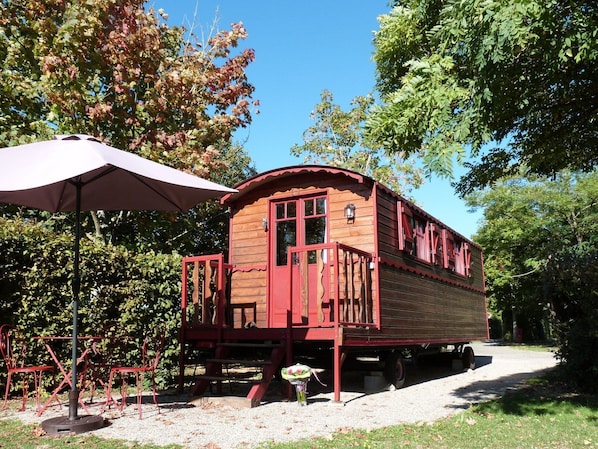 A wooden boat-shaped building with a deck and a covered seating area with chairs.
