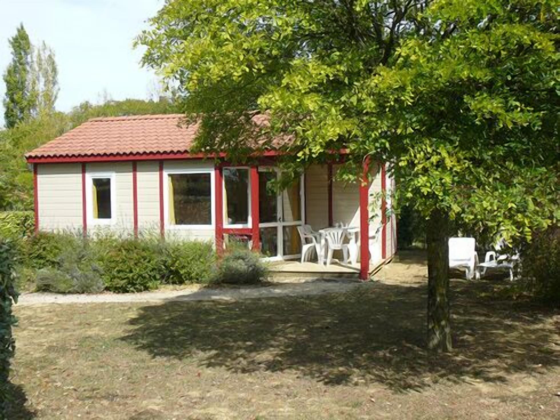 A small, single-story building with a red-tiled roof and a porch with white plastic chairs.